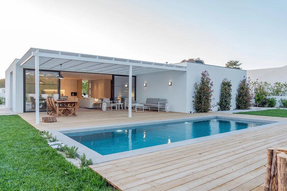 Modern beyaz bir evin ahşap verandası önünde yüzme havuzu ve çim bahçe