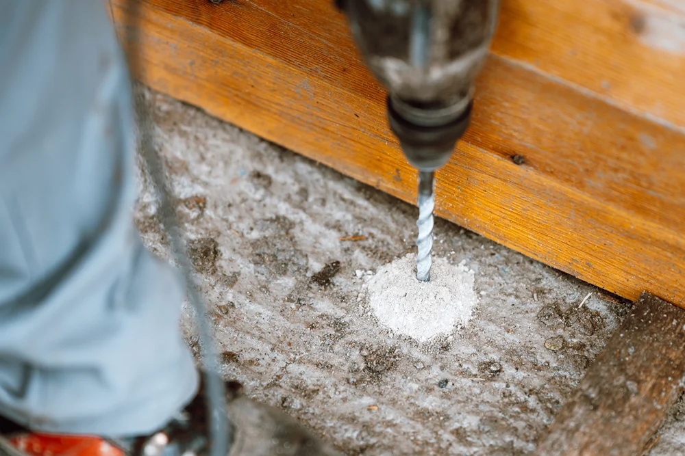 Beton zeminde ahşap bir tahtaya matkapla delik açılıyor