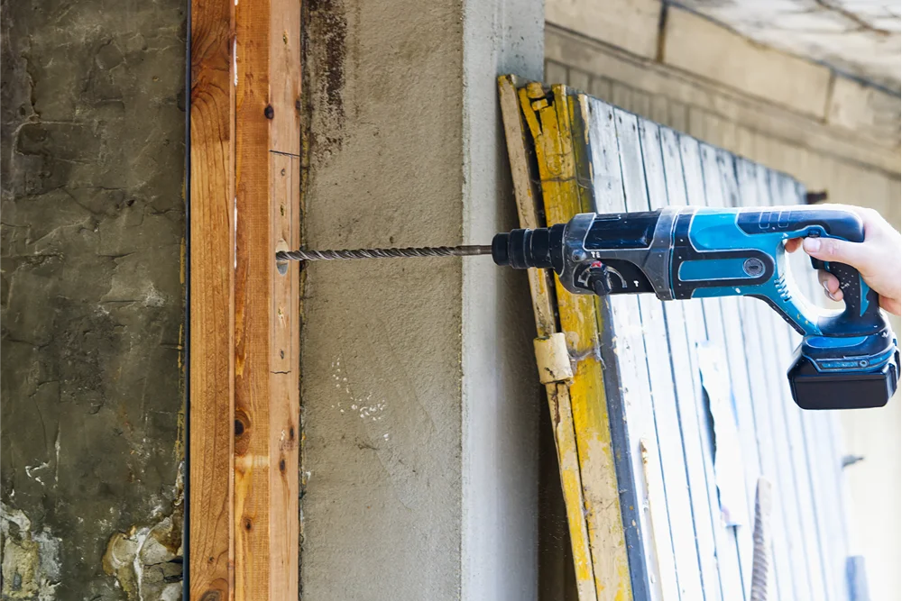 Beton duvarı delen bir kişi, akülü darbeli matkap kullanıyor